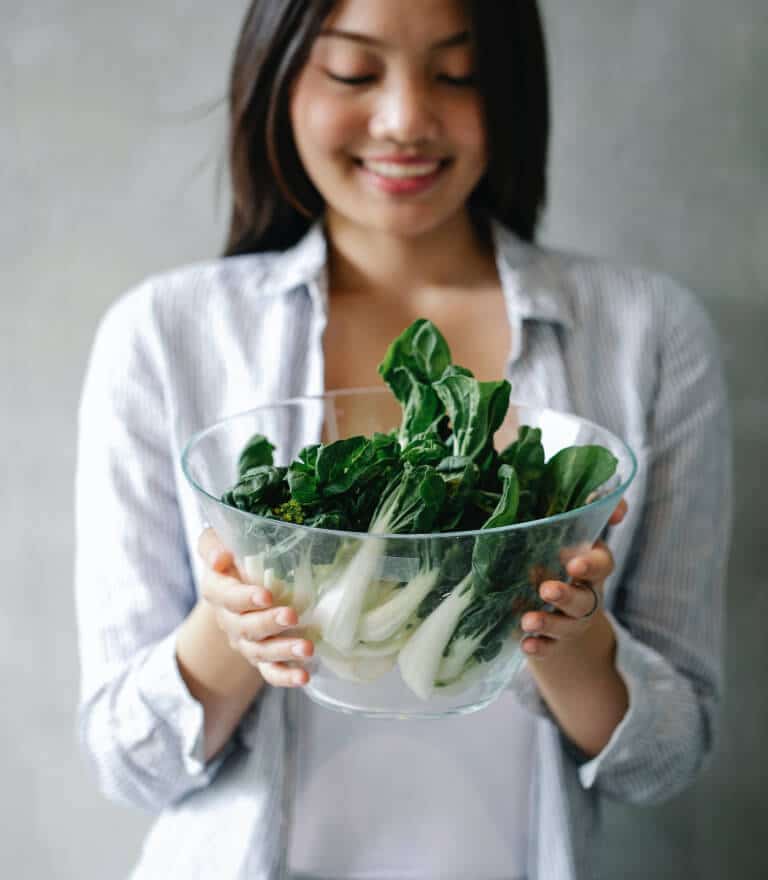 Fresh organic greens held by smiling woman, healthy eating, nutritious vegetables for wellness, Dr. Rebecca McAllister's health advice, clean eating lifestyle.