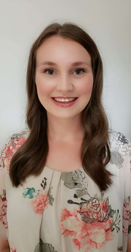 Smiling woman with long brown hair, floral blouse, and friendly expression.