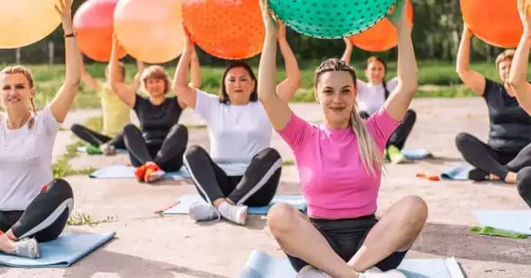 Women practicing yoga outdoors with large exercise balls for back health.