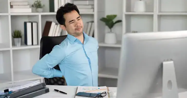 Man experiencing back pain at desk, demonstrating muscle discomfort relief.