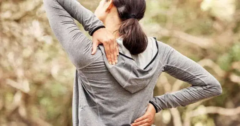 Woman holding her neck and back, experiencing discomfort in nature.