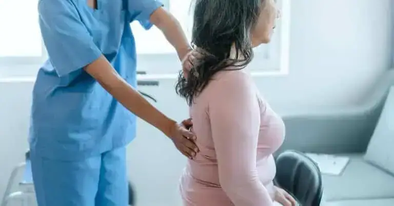 Medical professional examining a woman for low back pain in a clinical setting.