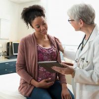 Pregnant woman talking with a chiropractor about their lower back pain Pregnant woman with doctor in a consultation, healthcare, prenatal care, obstetrics, gynecology.